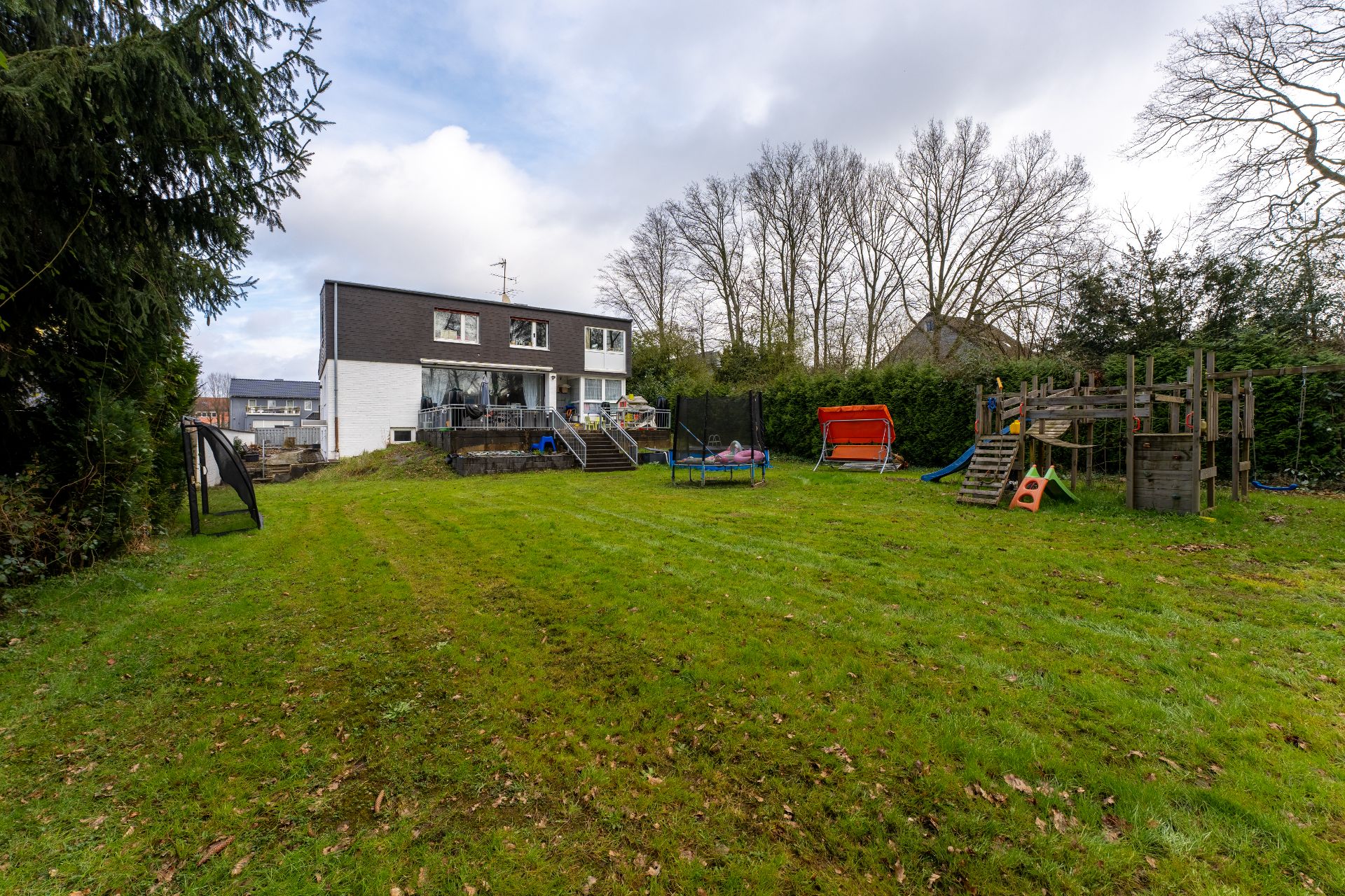 Großer Garten mit Spielplatz, Trampolin und Schaukel hinter einem Wohnhaus.