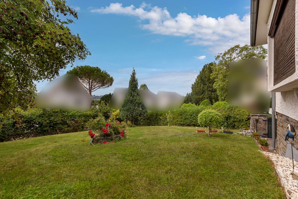 Grüner Garten mit Rasen, Blumenbeet und Sträuchern neben einem Wohnhaus an einem sonnigen Tag.