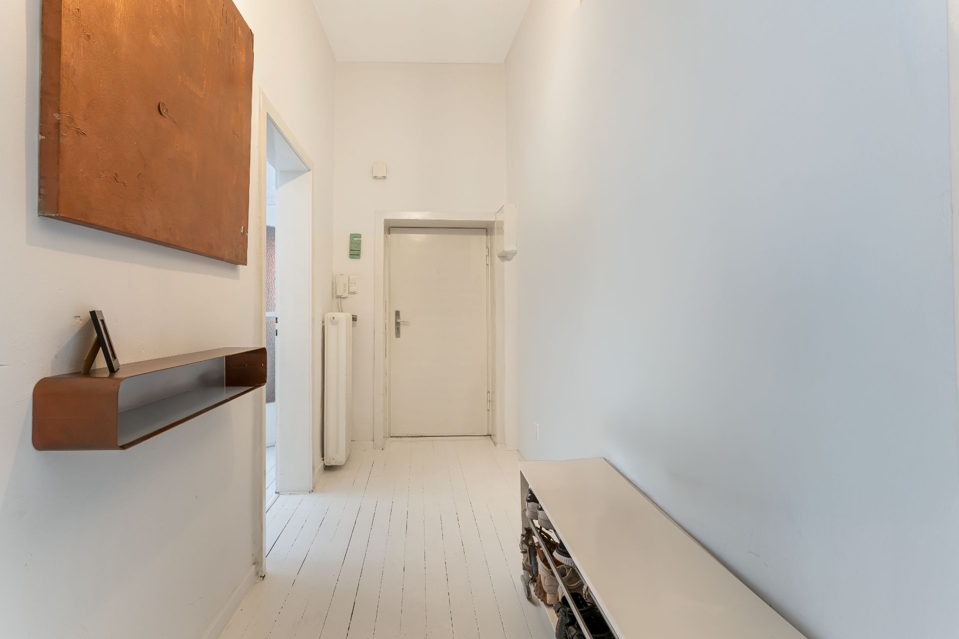 Heller Flur mit weißer Tür, Regal, Schuhablage und großem Bild an der Wand.