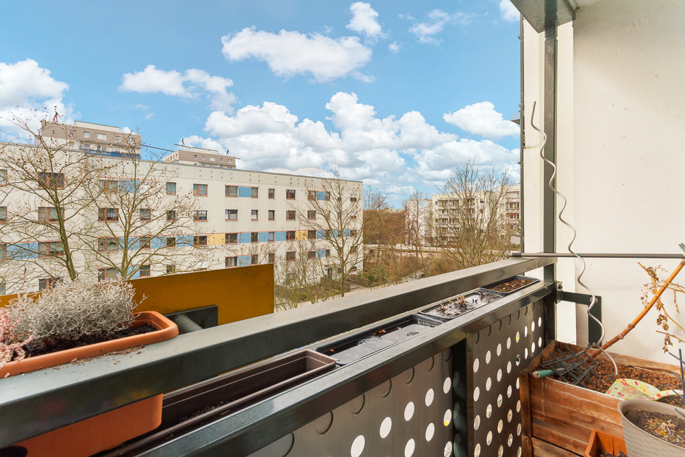 Blick von einem Balkon mit Pflanzen auf Wohngebäude und Bäume bei Tageslicht.
