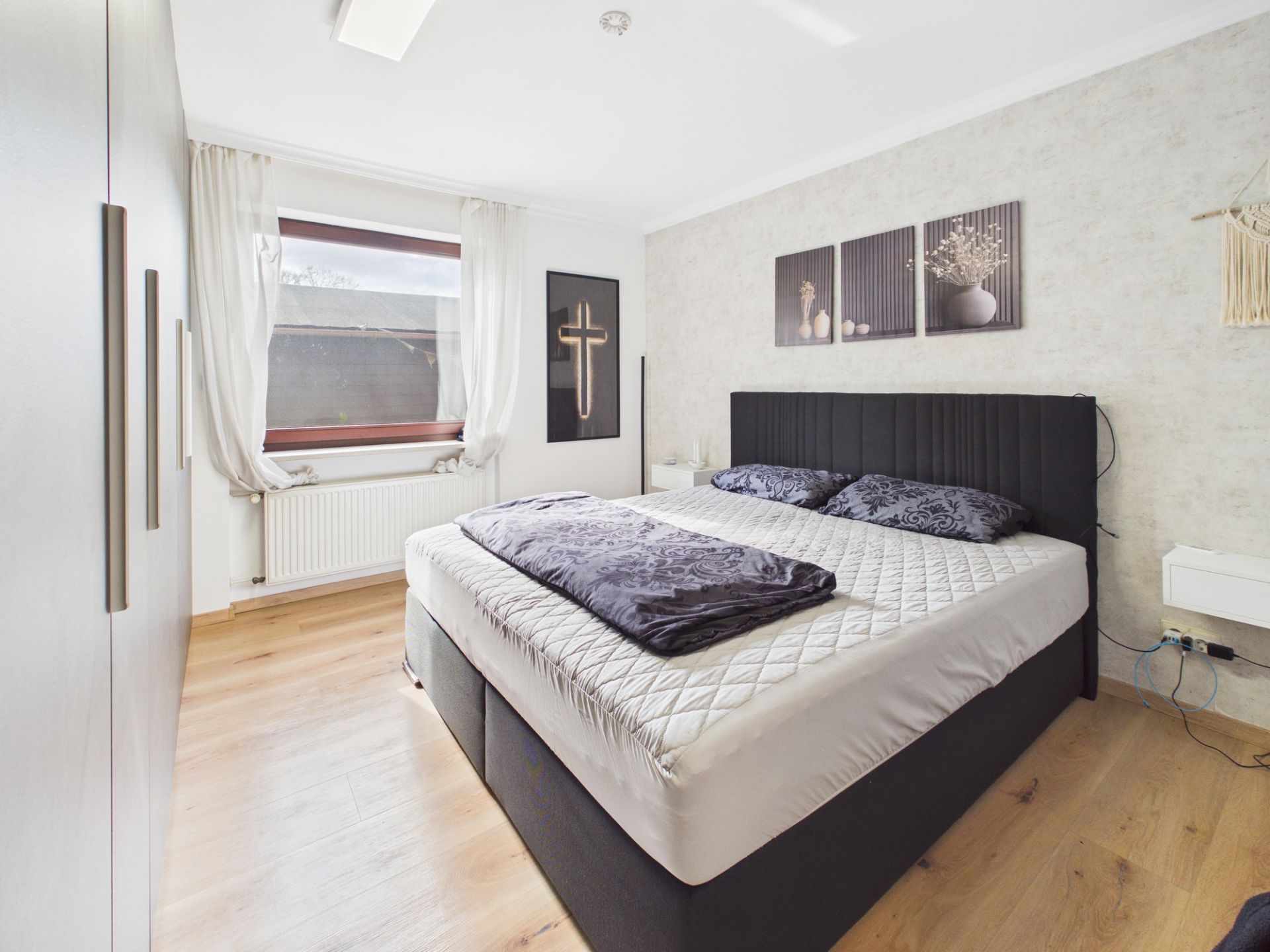 Modernes Schlafzimmer mit großem Bett, Holzfußboden, Fenstern und Wanddekoration.