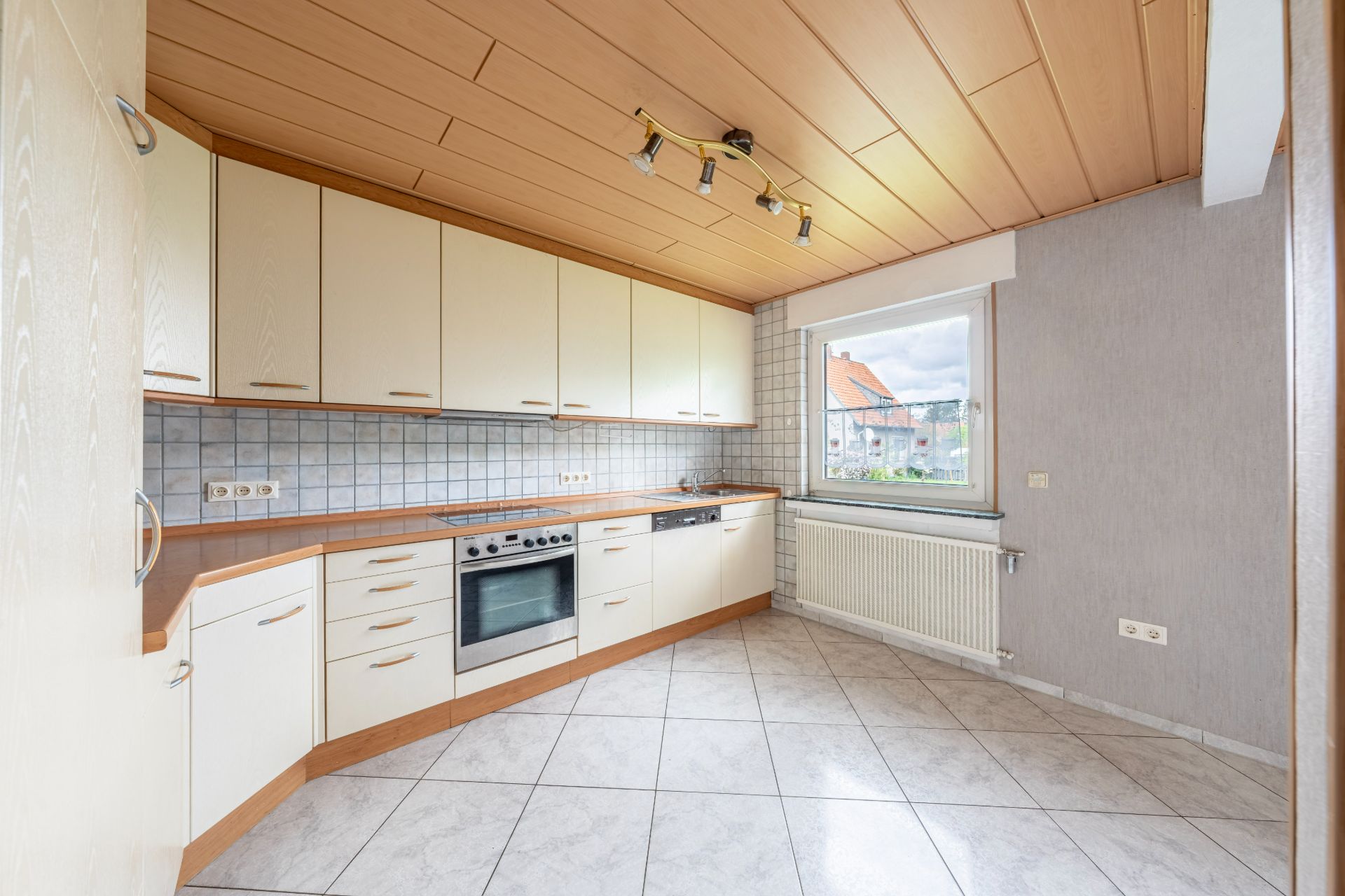 Helle Einbauküche mit weißem Fliesenspiegel, Fenster, Herd und Ober- sowie Unterschränken.