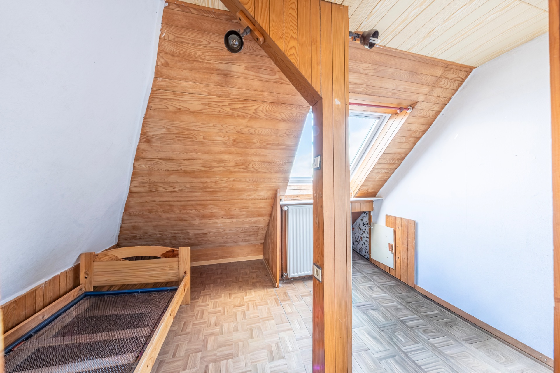 Dachzimmer mit Holzverkleidung, kleinem Bett und großem Dachfenster.