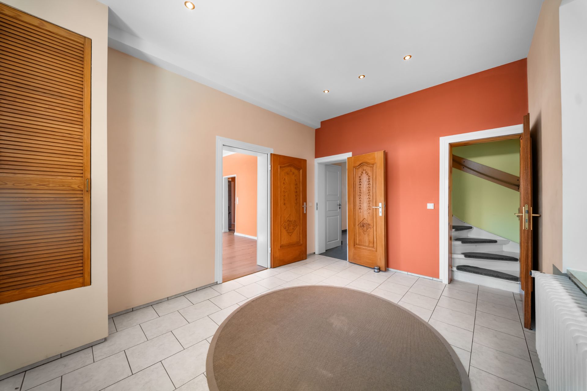 Heller Flur mit runder Matte, drei Holztüren und Treppe, Wände in Beige und Orange gestrichen.