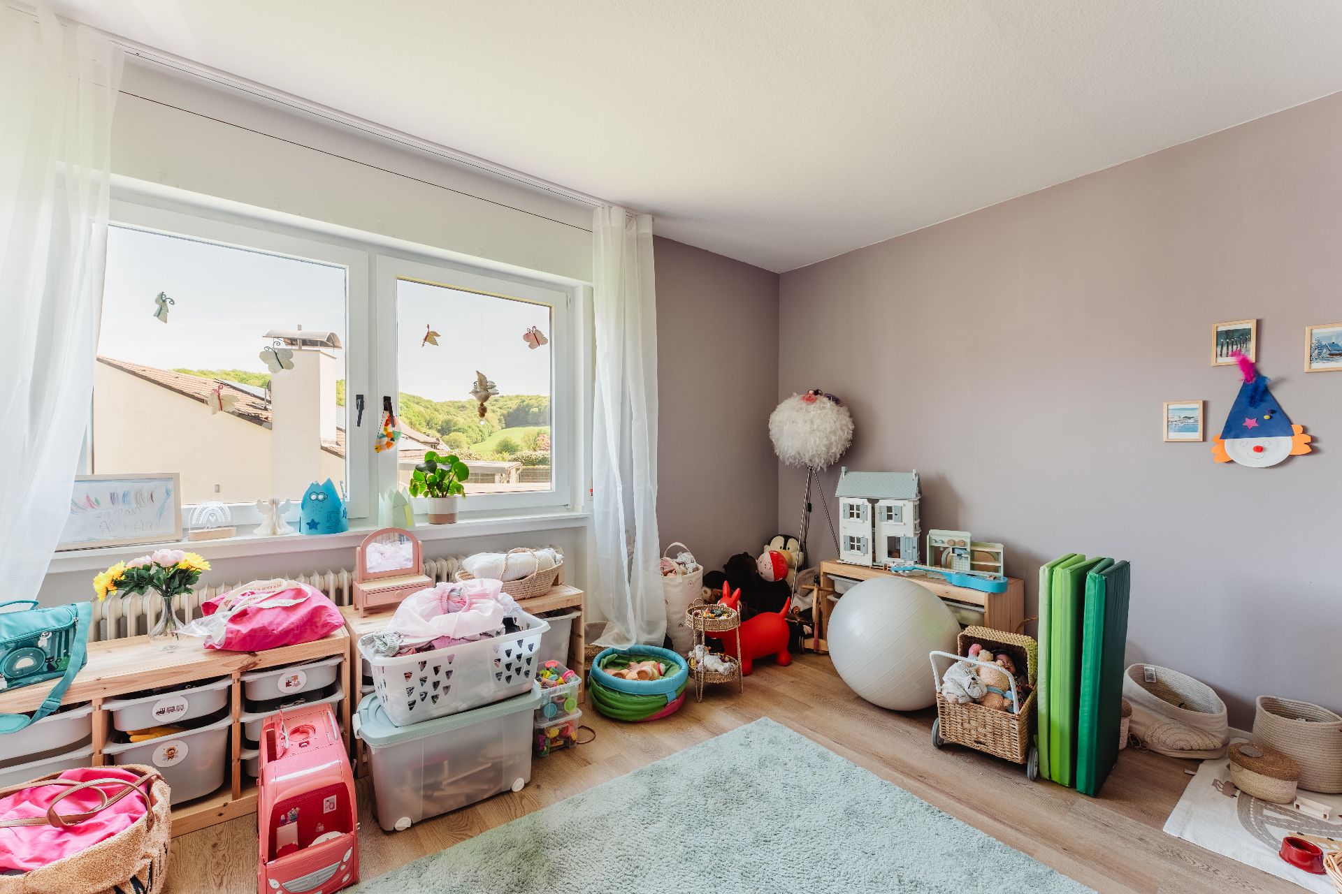 Helles Kinderzimmer mit Spielzeug, Aufbewahrungsboxen und großem Fenster mit Blick nach draußen.