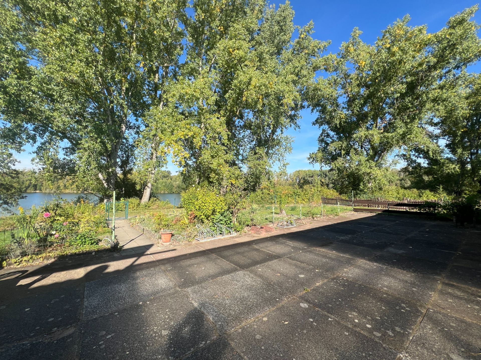 Große Terrasse mit Blick auf Garten, Bäume und einen See im Hintergrund.