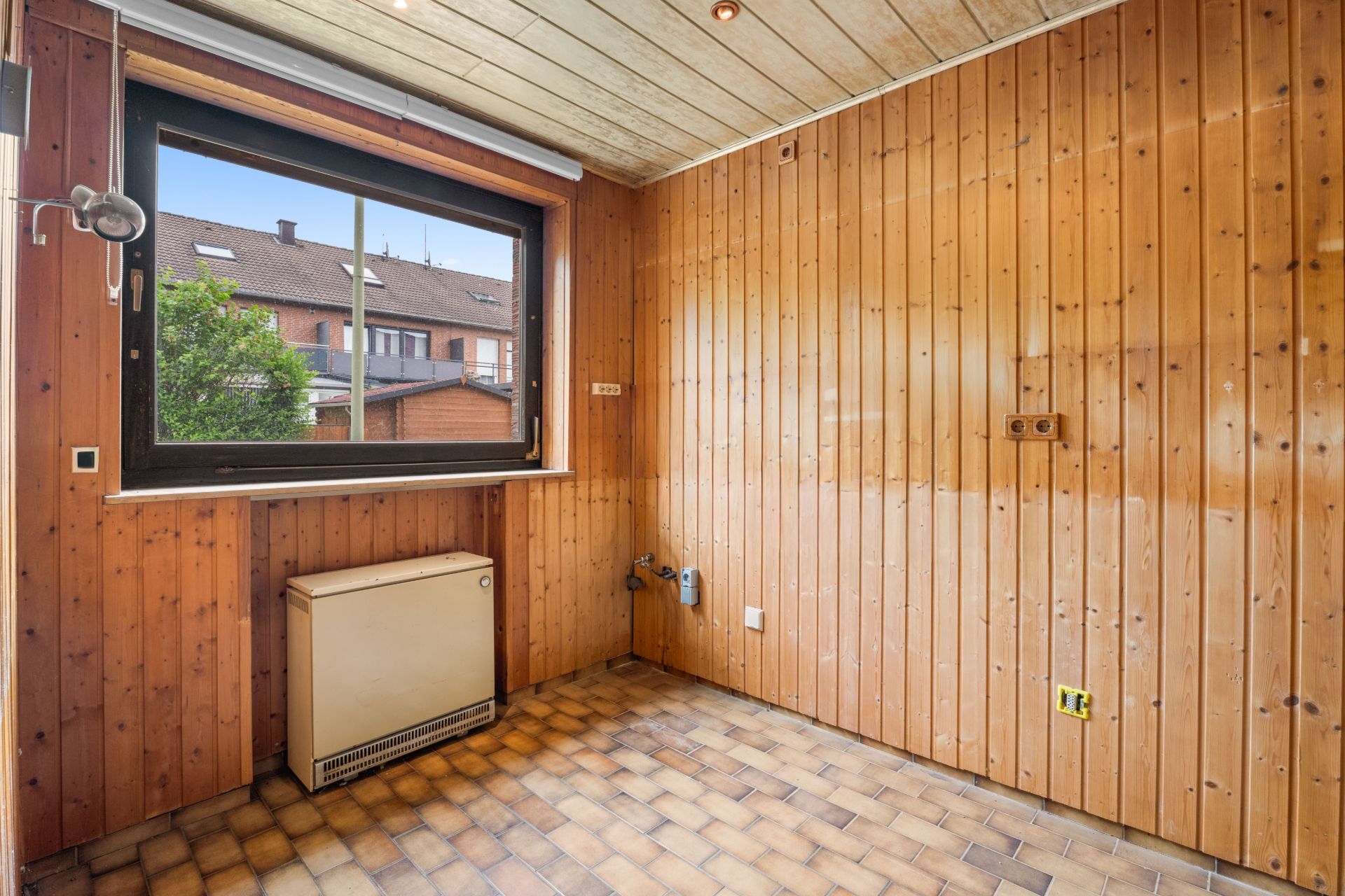Leerer Raum mit Holzverkleidung, großem Fenster und Fliesenboden.