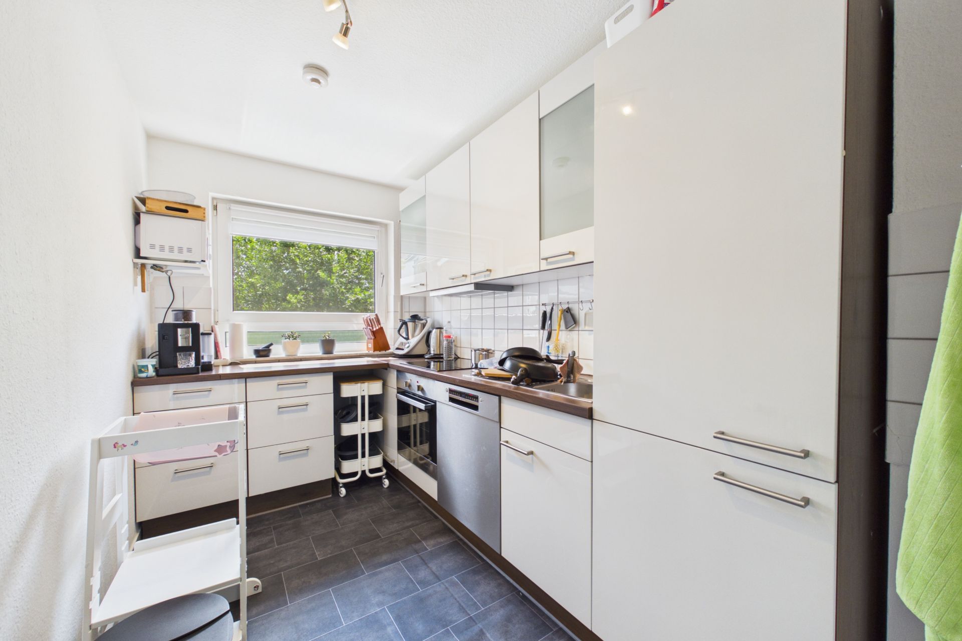 Moderne, helle Einbauküche mit Fenstern, weißen Schränken und dunklem Boden.