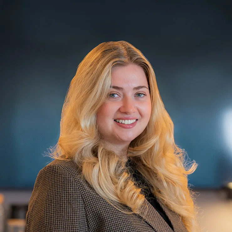 Eine lächelnde Frau mit langen, blonden Haaren trägt einen beigen Blazer und ein schwarzes Shirt.