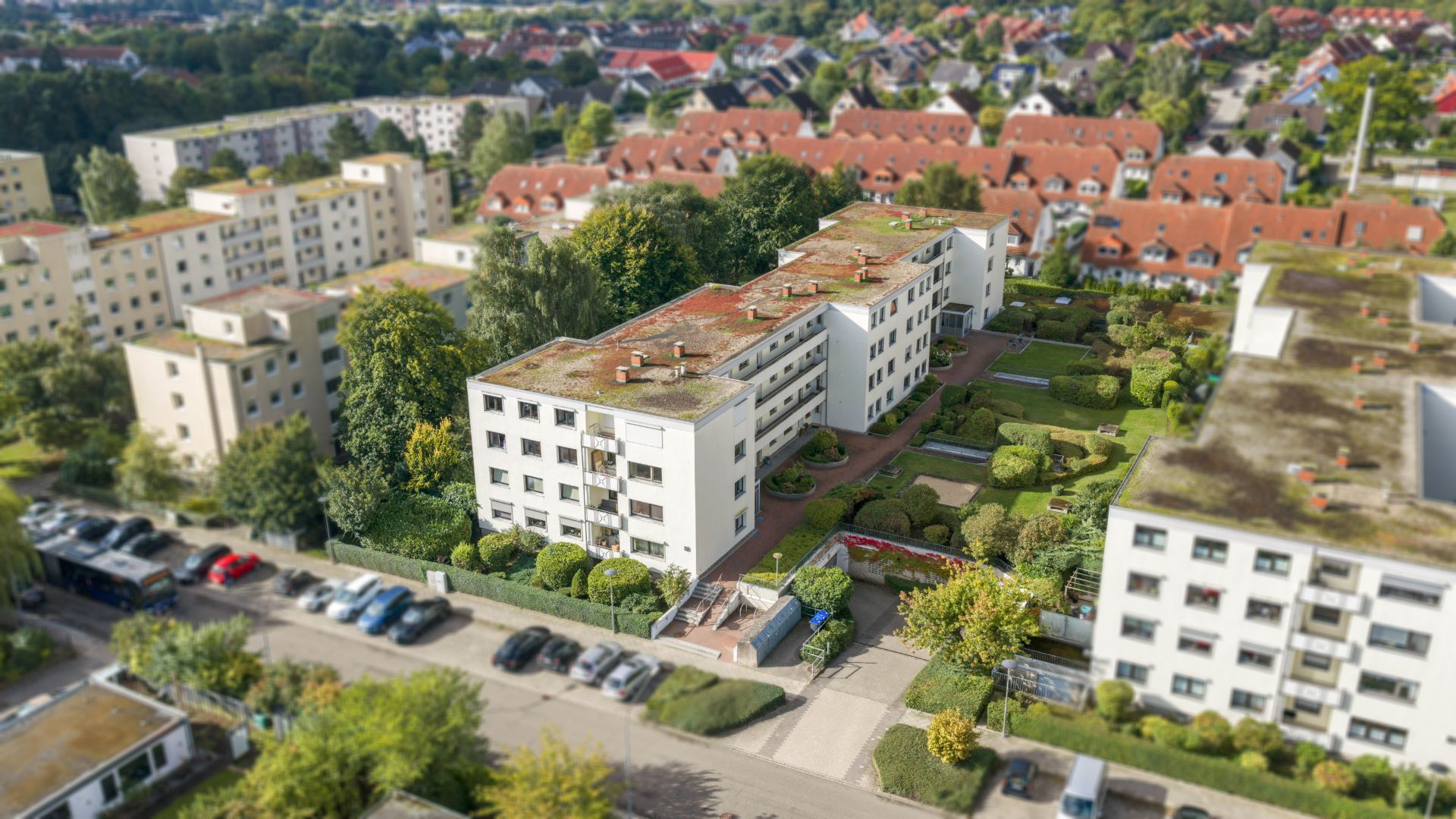 Luftaufnahme von mehreren Wohngebäuden mit begrünten Höfen und parkenden Autos.