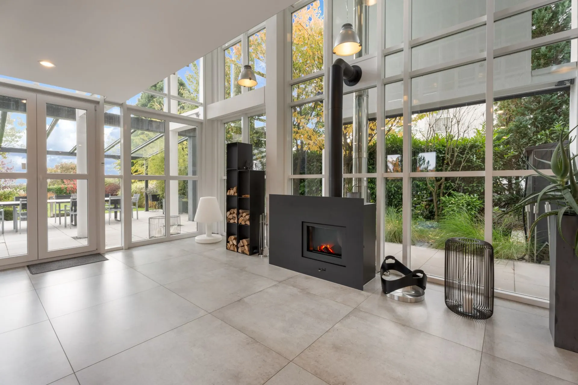 Wohnzimmer mit Kamin, großen Fenstern und Blick auf den Garten.