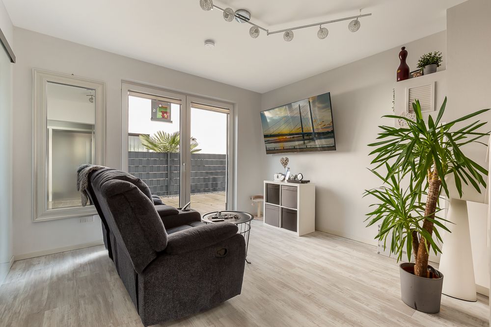 Modernes Wohnzimmer mit grauem Sofa, großem Spiegel, Fernseher und Zimmerpflanze, Blick auf Terrasse.