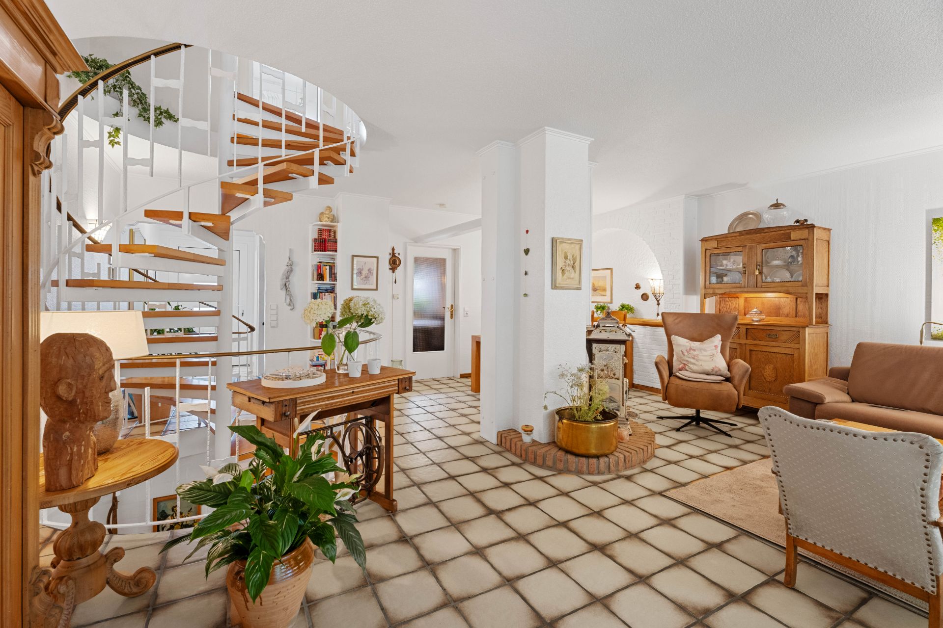 Helles Wohnzimmer mit Wendeltreppe, Holzmöbeln, Sessel, Sofa und vielen Pflanzen.