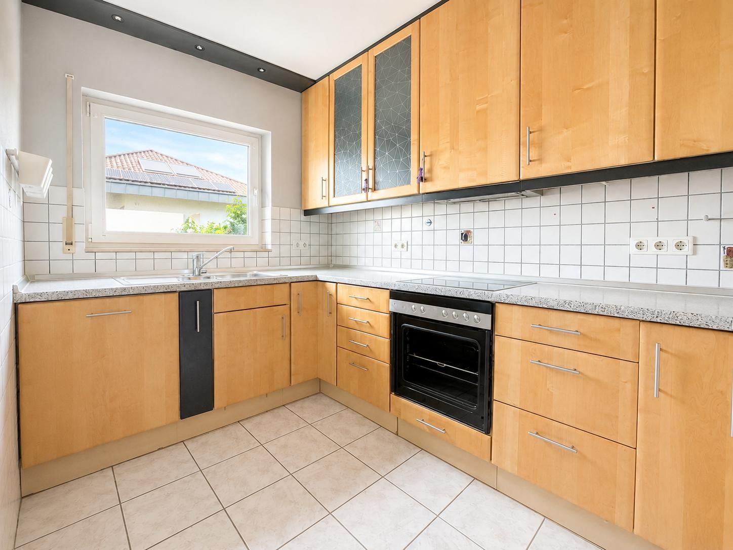 Helle Einbauküche mit Holzfronten, Herd, Spüle und Fenster, moderne Fliesen an Wand und Boden.