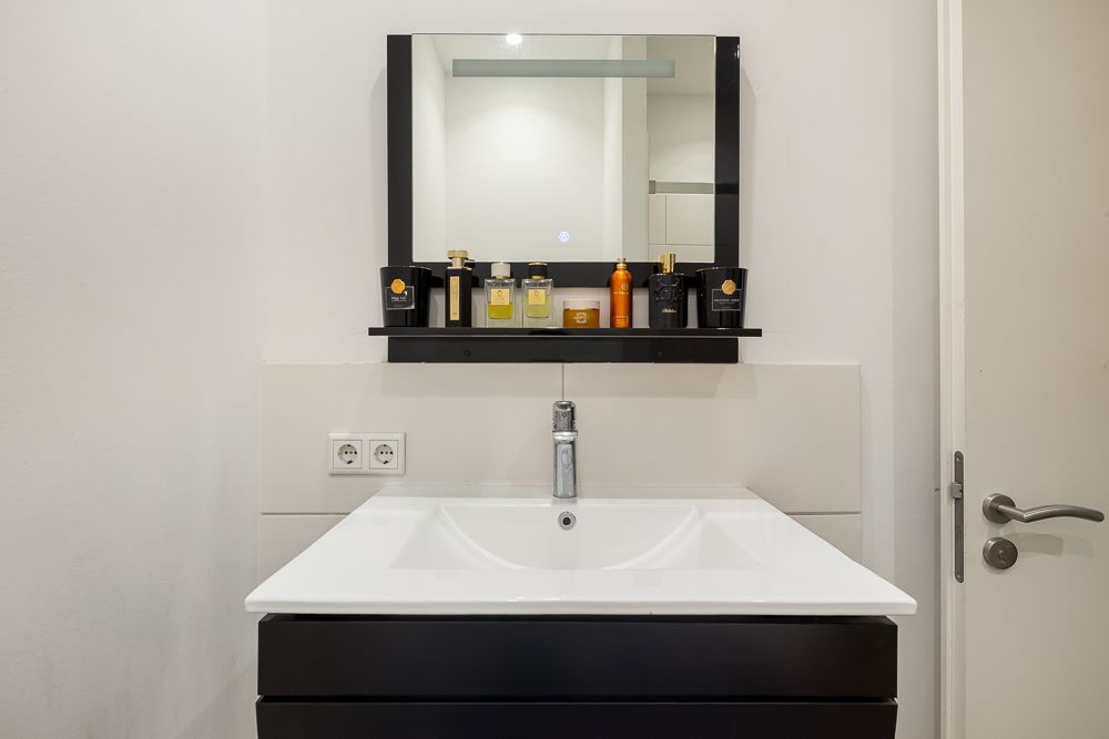 Waschbecken mit Spiegel und verschiedenen Flaschen auf einem Regal im Badezimmer.