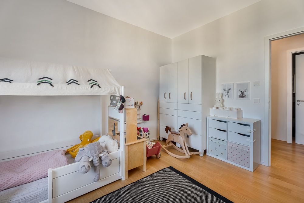Helles Kinderzimmer mit Bett, Spielzeug, Schrank und Kommode auf Holzfußboden.