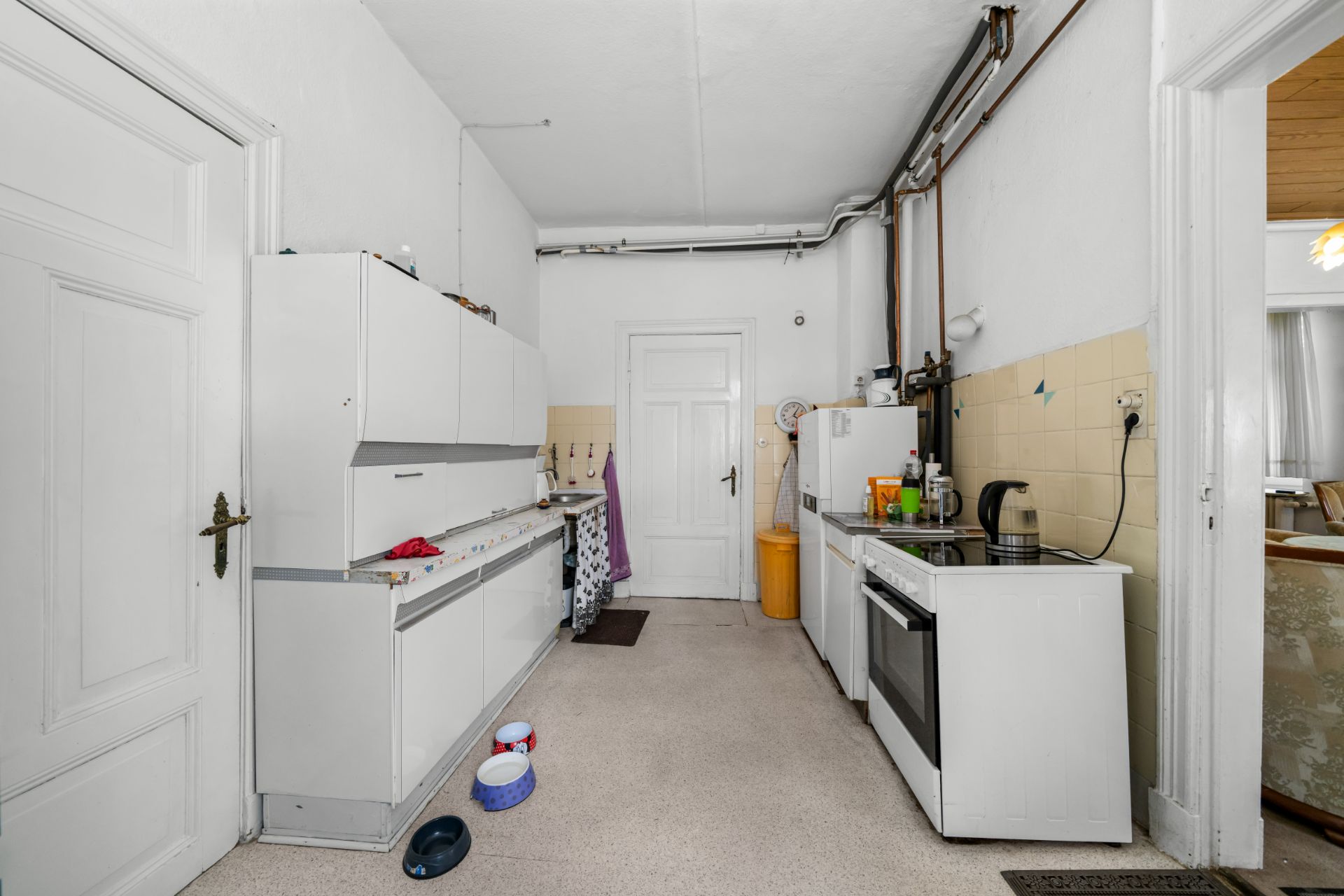 Schlichte Küche mit weißen Schränken, Herd, Kühlschrank und Haushaltsgegenständen.