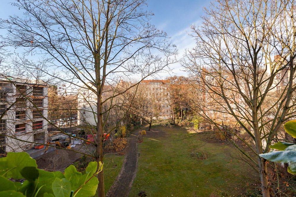 Blick auf einen begrünten Innenhof mit Bäumen und Gehweg, umgeben von Wohngebäuden.