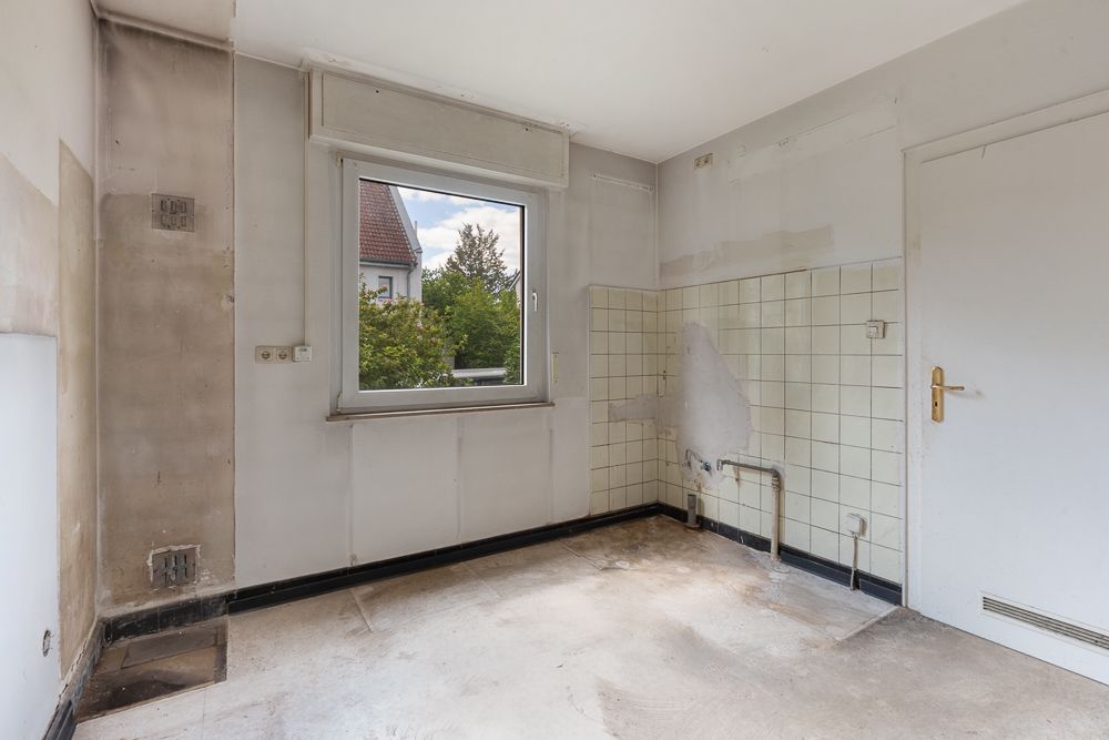 Leerer Raum mit Fenster, weißen Wänden, Fliesen an einer Wand und sichtbaren Wasseranschlüssen.