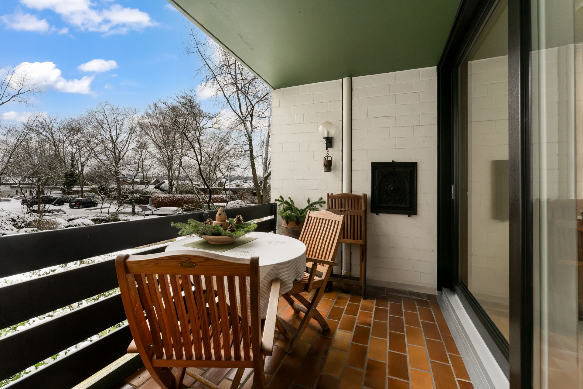 Balkon mit Holztisch, vier Stühlen und Blick auf winterliche Bäume.