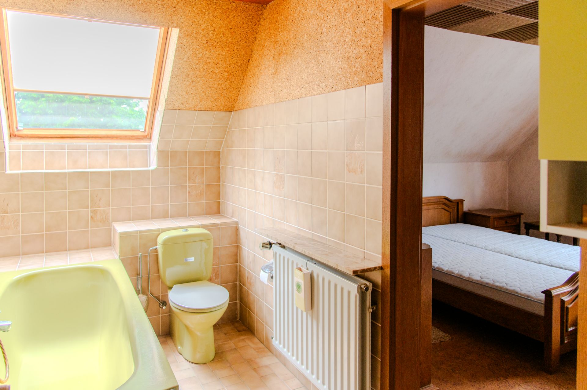 Badezimmer mit gelber Badewanne, Toilette und offenem Zugang zu einem Schlafzimmer mit Bett.