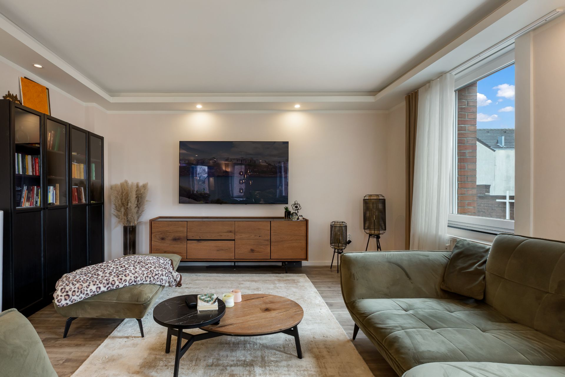 Modernes Wohnzimmer mit grünem Sofa, Couchtisch, TV, Regal und großem Fenster.