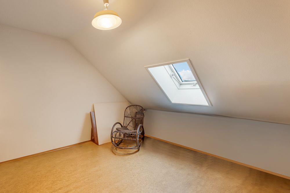 Dachzimmer mit Schrägdecke, Dachfenster und einem Holzschaukelstuhl.