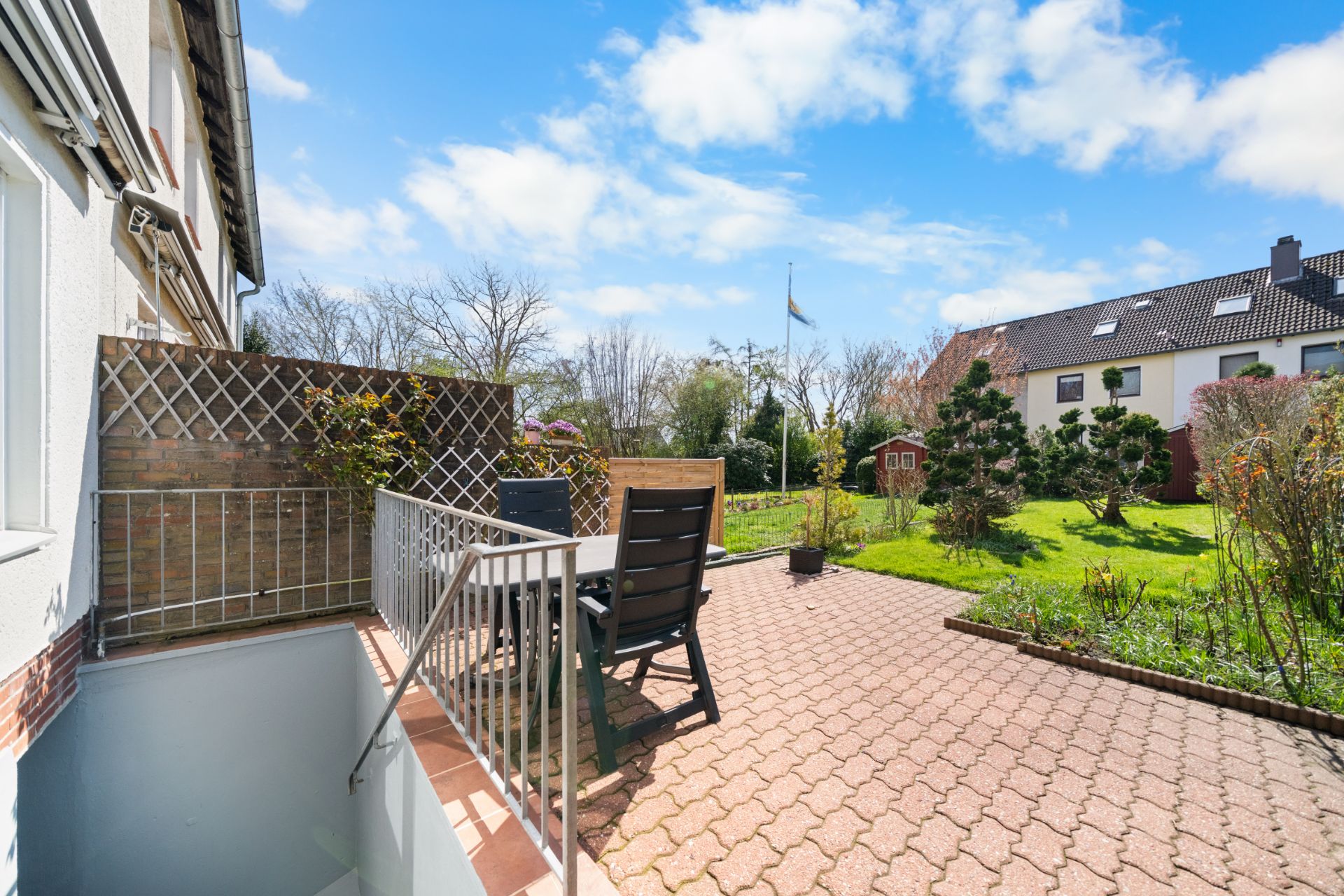 Gepflasterte Terrasse mit Tisch und Stühlen, Blick auf Garten und Nachbarhäuser.