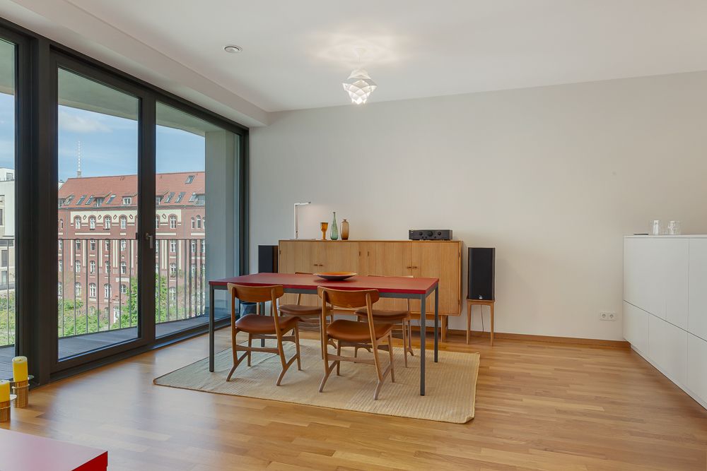 Essbereich mit Holztisch, vier Stühlen, Sideboard und großen Fenstern zu einem Balkon.