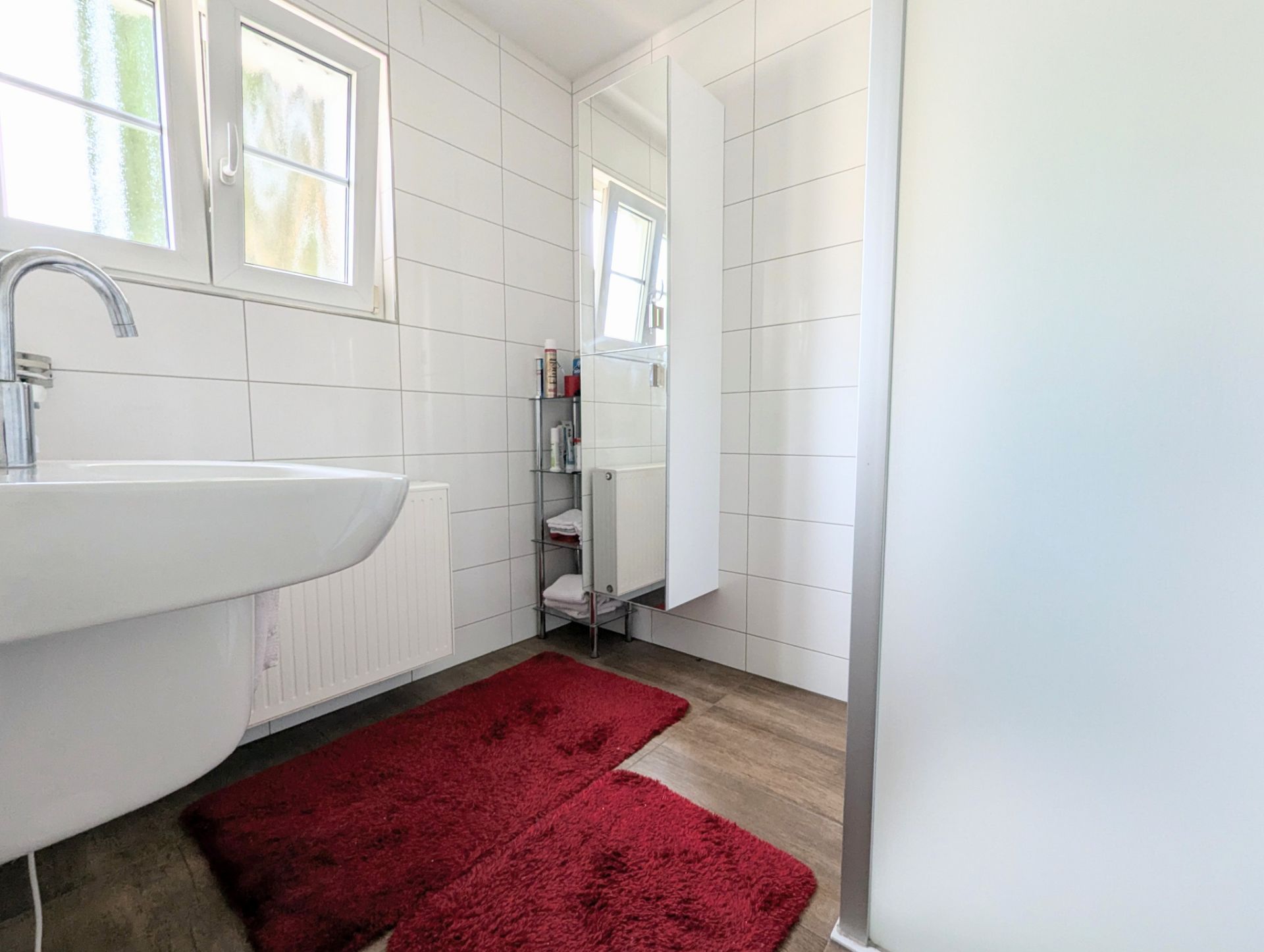 Helles Bad mit Waschbecken, Spiegel, roten Teppichen und weißen Fliesen.