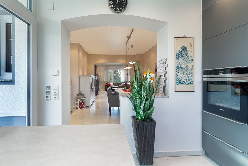 Blick von der Küche ins Wohnzimmer mit Pflanze, Uhr und Wandbild.