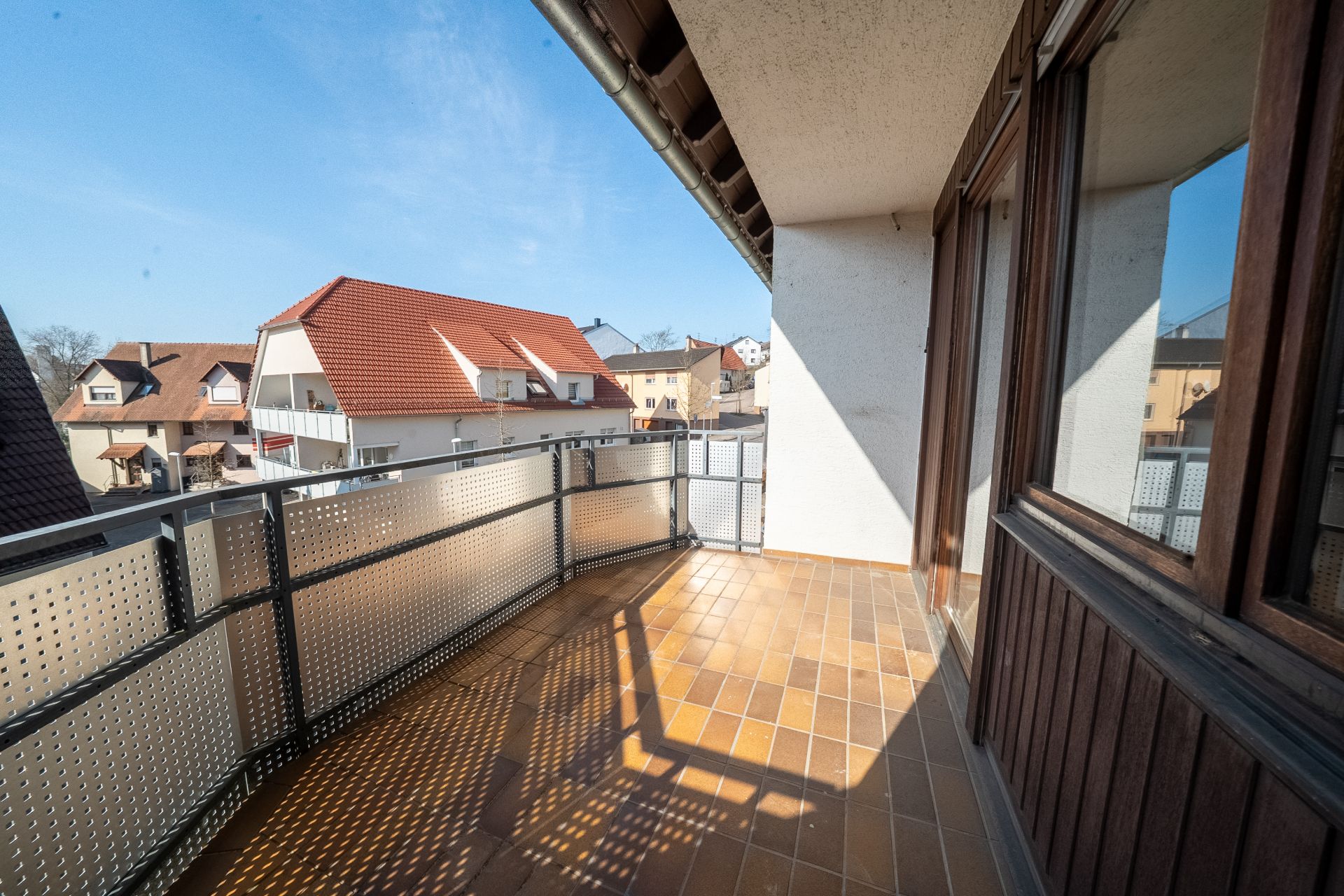 Balkon mit Fliesenboden und Metallgeländer, Blick auf Nachbarhäuser mit roten Dächern.