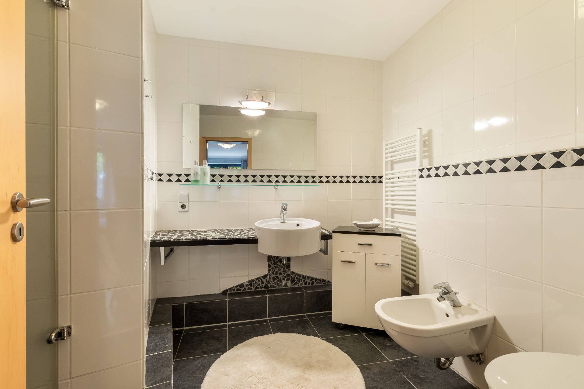 Modernes Bad mit Waschbecken, Spiegel, Bidet und weißen Fliesen.