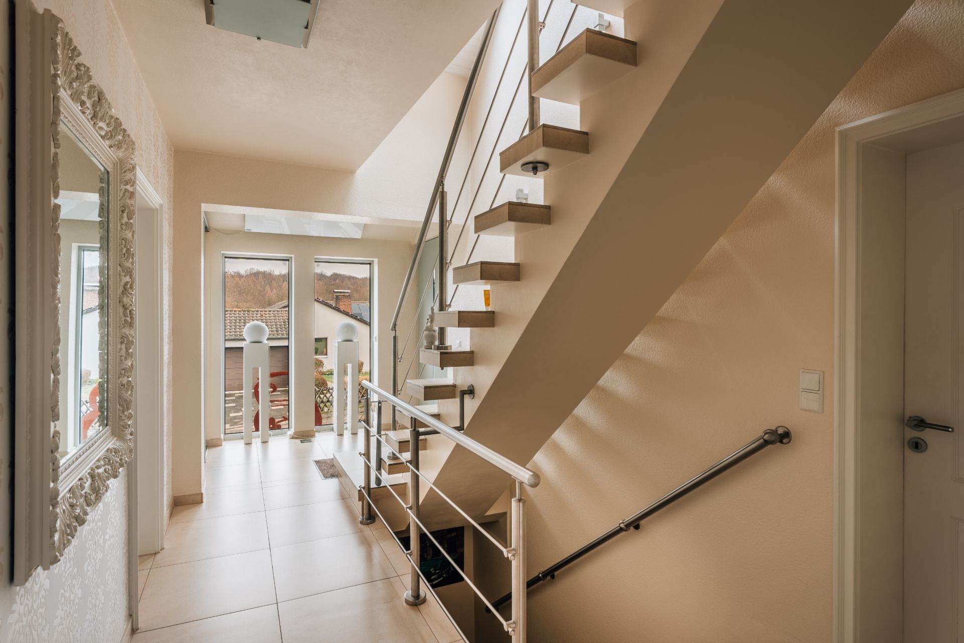 Heller Flur mit moderner Treppe, großem Spiegel und Blick auf einen Balkon.