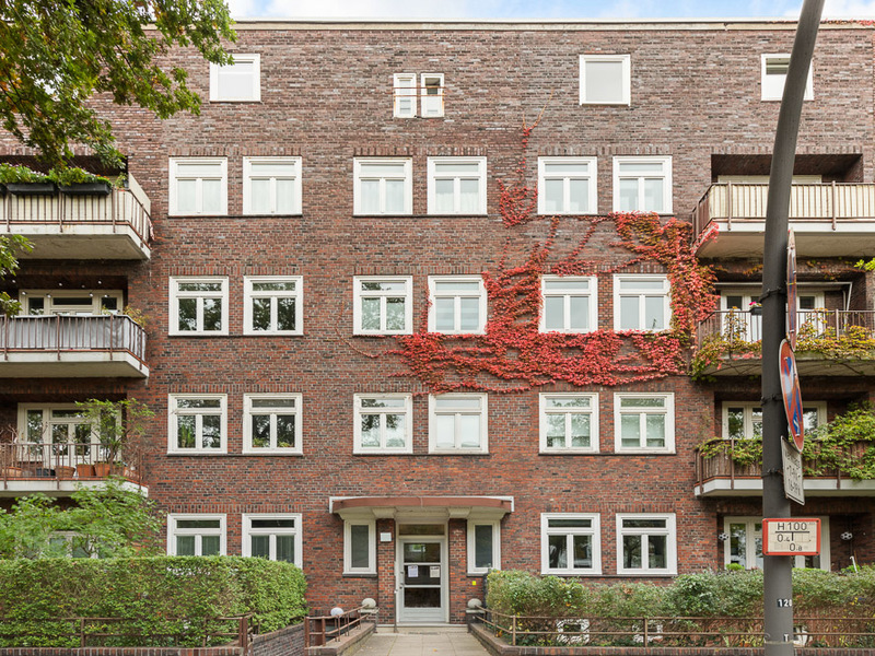 Wohngebäude aus rotem Klinker mit weißen Fenstern und Efeubewuchs an der Fassade.