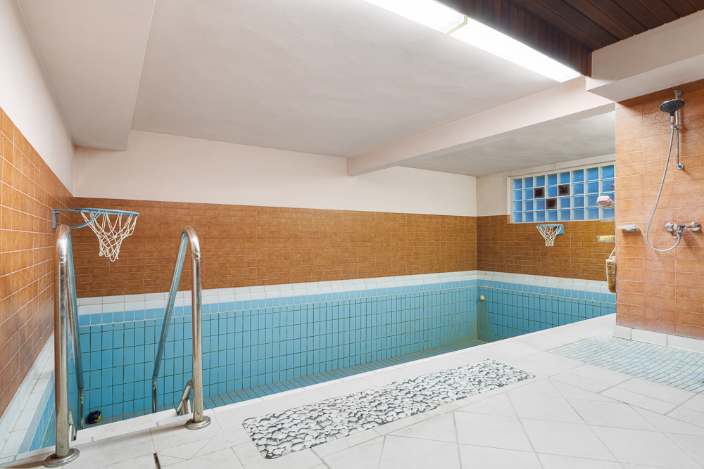 Innenpool mit blauen Fliesen, Basketballkörben und einer Dusche an der Wand.