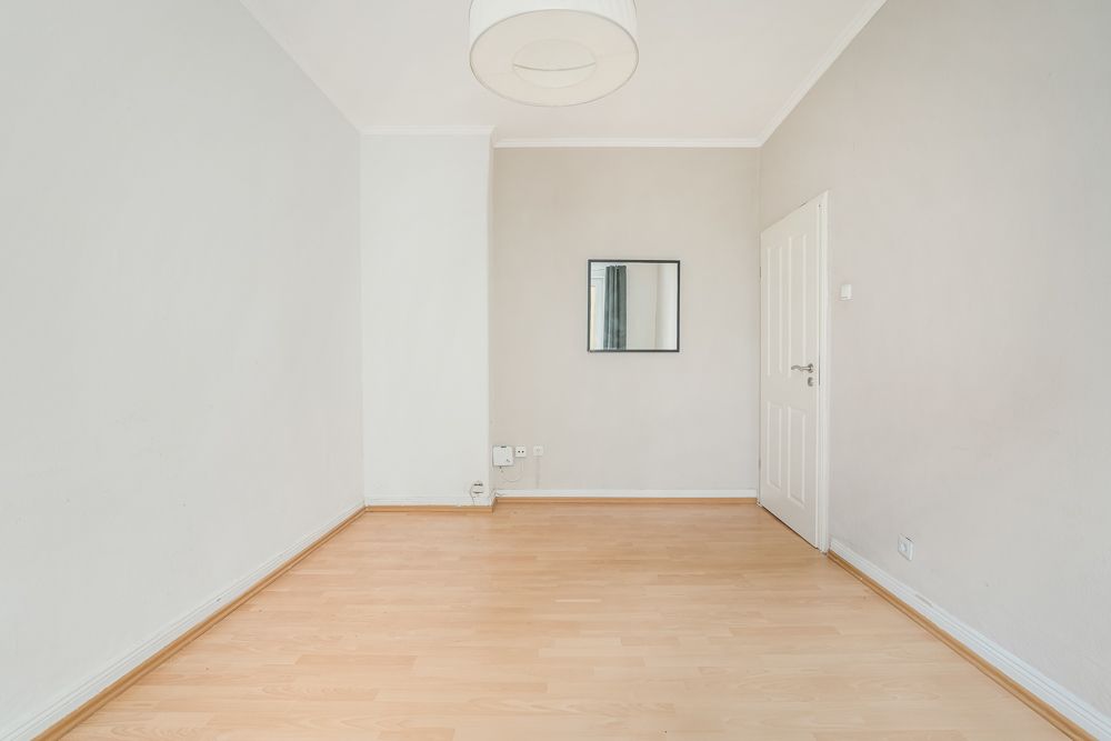 Leerer, heller Raum mit Holzboden, weißer Tür und Wandspiegel.