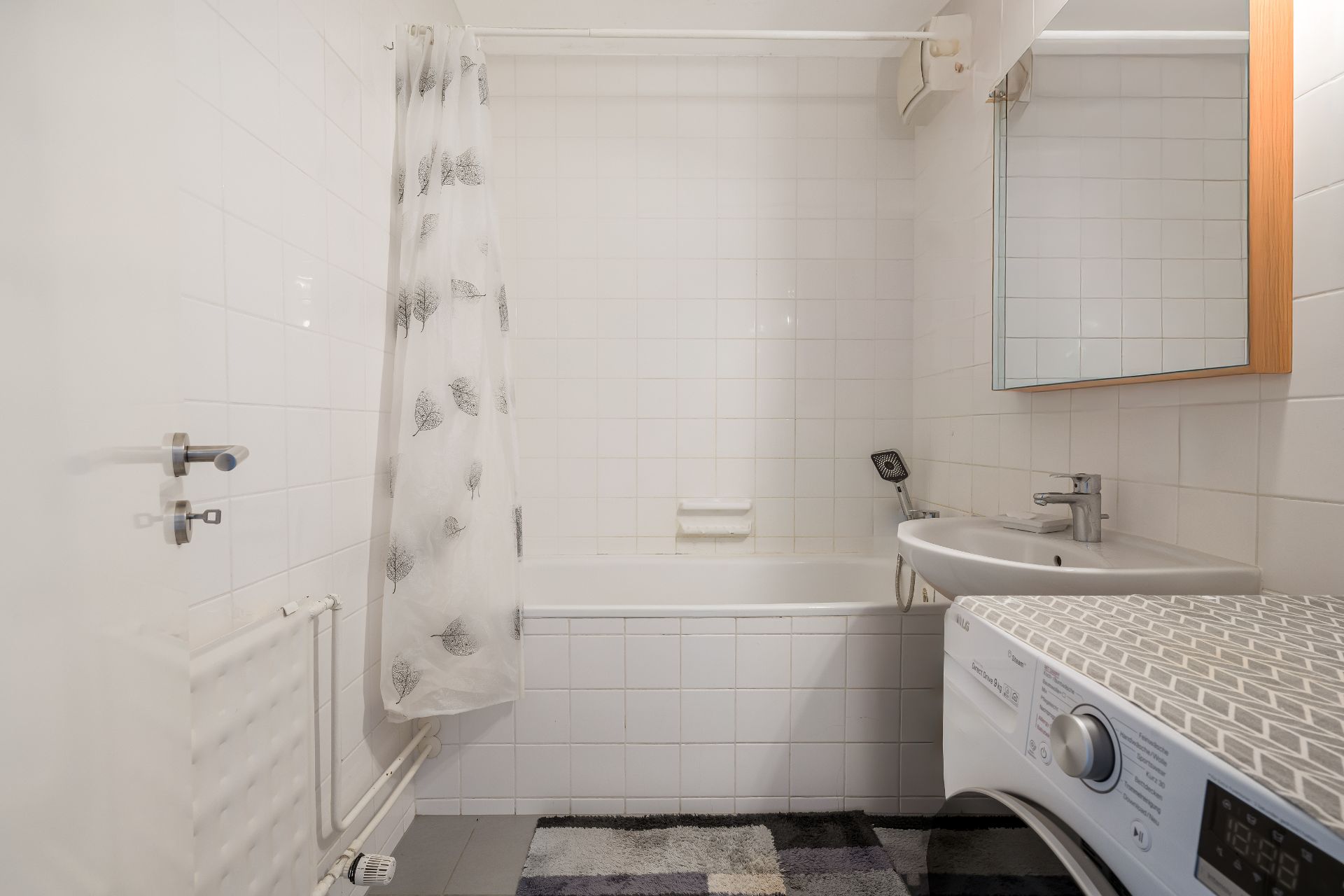 Helles Badezimmer mit Badewanne, Duschvorhang, Waschbecken, Spiegel und Waschmaschine.