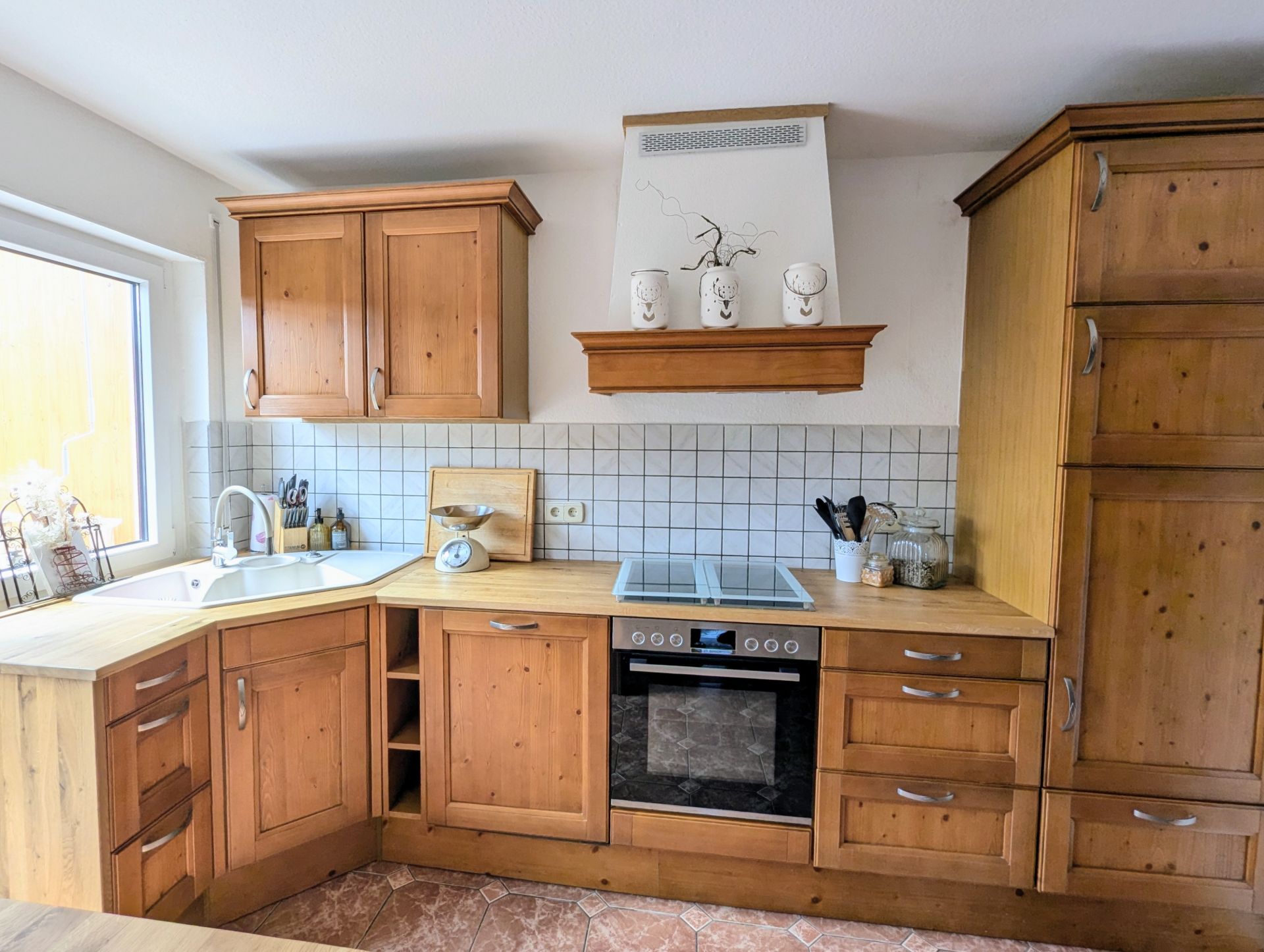 Helle Küche mit Holzschränken, Herd, Spüle und großem Fenster.