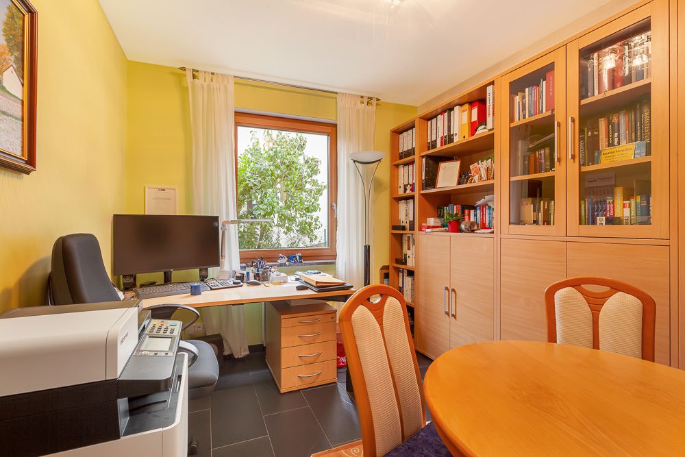 Helles Arbeitszimmer mit Schreibtisch, Computer, Bücherregal und rundem Esstisch.