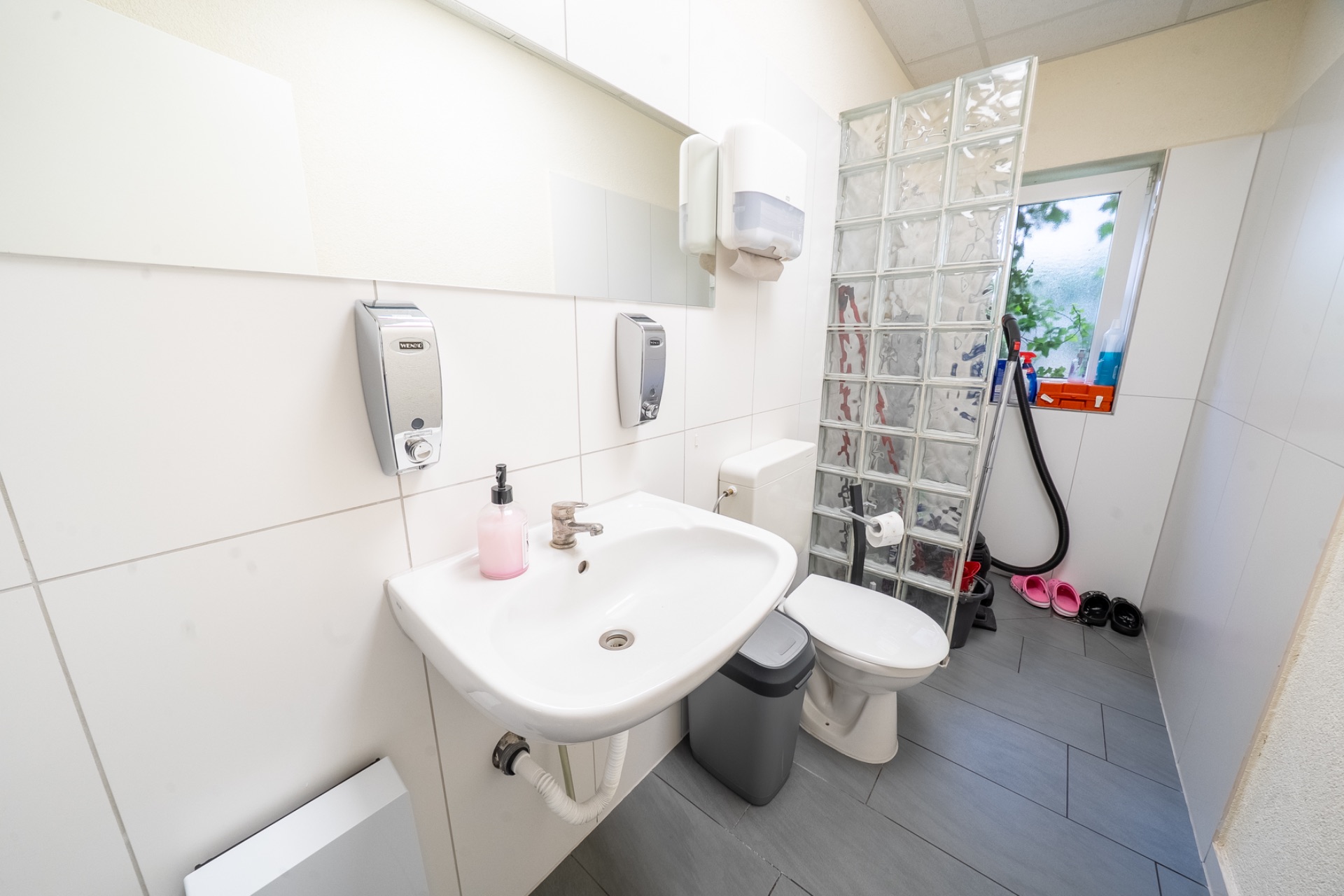 Modernes Badezimmer mit Waschbecken, Toilette, Glaswand, Fenster und Waschutensilien.