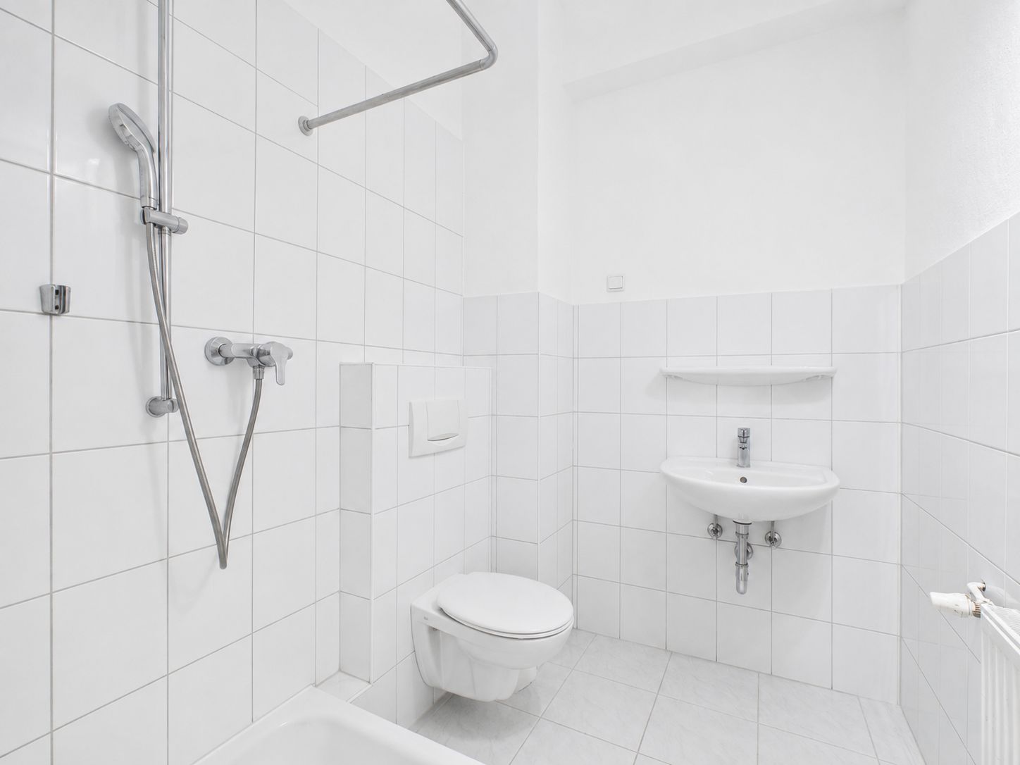 Weiß gefliestes Badezimmer mit Dusche, WC und Waschbecken.
