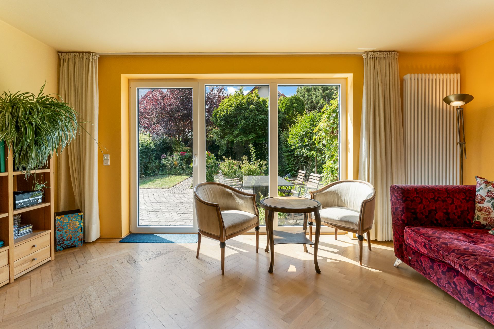 Wohnzimmer mit gelben Wänden, zwei Sesseln und Glastür zum Garten.