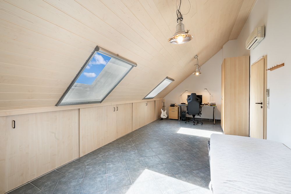 Helles Dachzimmer mit Schreibtisch, Stuhl, Bett, Kleiderschrank und Dachfenstern.