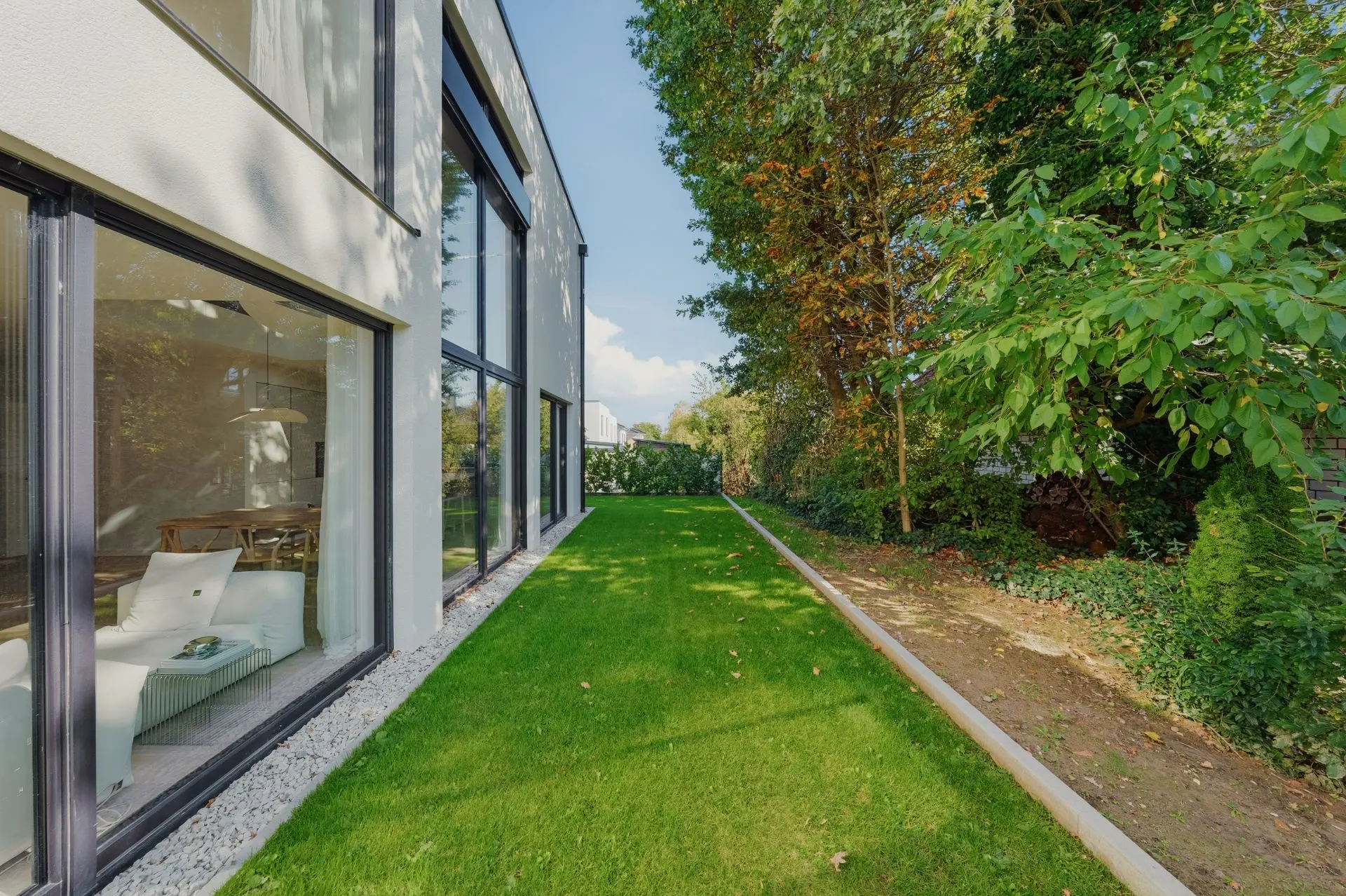 Moderner Wohnbereich mit großer Fensterfront und Blick auf einen gepflegten Garten mit Rasenfläche.
