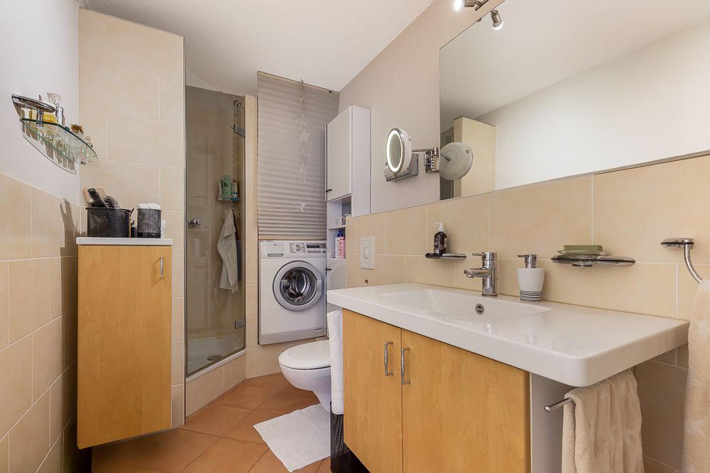 Modernes Badezimmer mit Dusche, Waschbecken, Waschmaschine und Holzschränken.