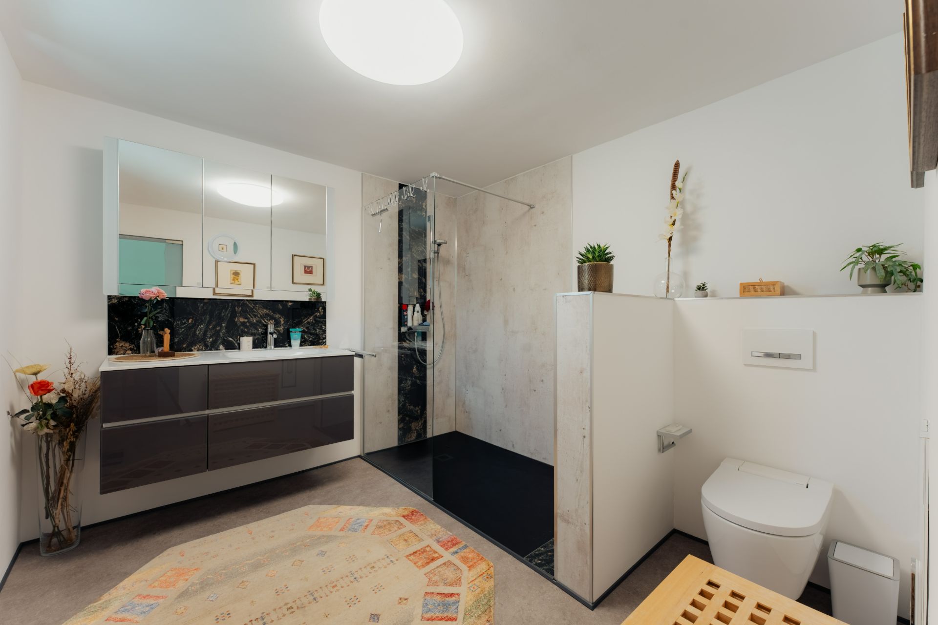Modernes Badezimmer mit großer Dusche, Waschtisch, Spiegel und Dekopflanzen.