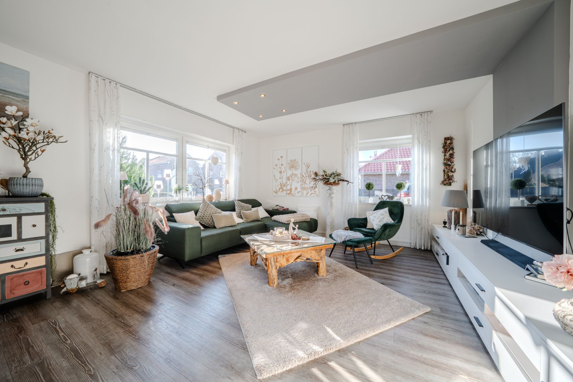 Helles Wohnzimmer mit grünem Sofa, Holz-Couchtisch und großem Fernseher auf weißem Sideboard.