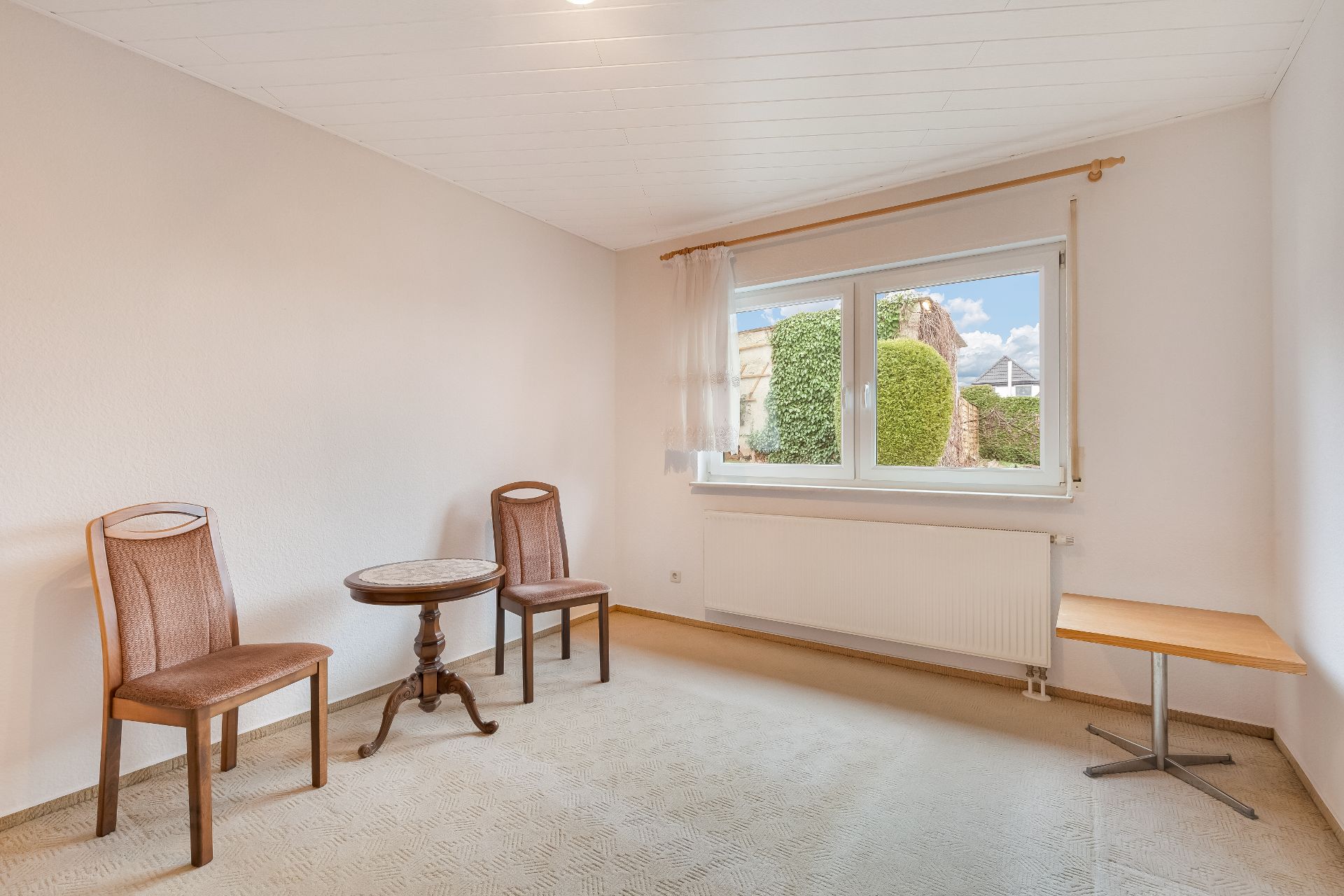 Helles Zimmer mit zwei Stühlen, kleinem Tisch und großem Fenster mit Blick ins Grüne.