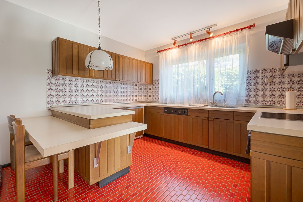 Küche mit roten Fliesen, Holzschränken, Esstisch, großem Fenster und gemusterter Fliesenwand.